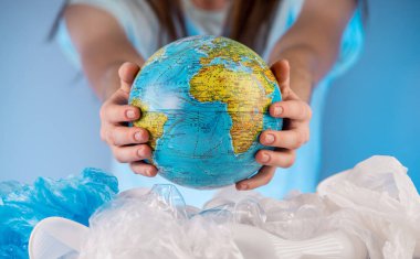 Bir kadın plastik bir çöp yığını içinde bir Dünya 'yı söküyor. Çevre kirliliği ve gezegeni kurtarma kavramı