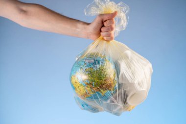 Bir insan elinde Dünya şeklinde bir çöp torbası ve elinde bir plastik tutuyor. Çevre kirliliği ve gezegeni kurtarma kavramı