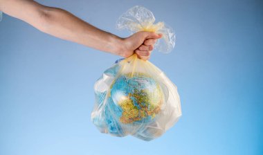 Bir insan elinde Dünya şeklinde bir çöp torbası ve elinde bir plastik tutuyor. Çevre kirliliği ve gezegeni kurtarma kavramı