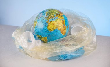 Plastik çöplerin arasında çöp torbasında küre şeklinde bir dünya. Çevre kirliliği ve gezegeni kurtarma kavramı