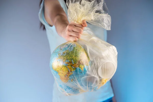 A person is holding a garbage bag with Earth in the form of a globe and plastic in his hand. Concept of environmental pollution and saving the planet