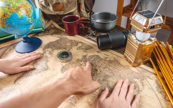 観光客の手は 世界地図上の場所を指しているとキャンプ用品と木製のテーブルの上に次の旅行のための場所を選択します 旅と発見の概念 — ストック写真