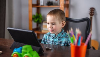 Gömlekli küçük çocuk tablet ekranına bakıyor. Mesafe eğitimi ve boş zaman kavramı