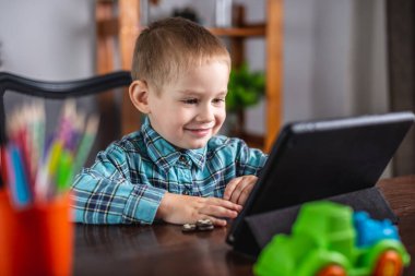 Gömlekli küçük çocuk tablet ekranına bakıyor. Mesafe eğitimi ve boş zaman kavramı
