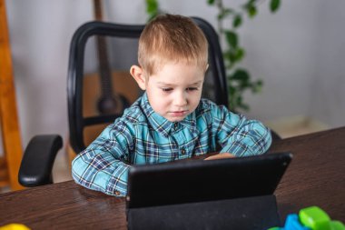 Gömlekli küçük çocuk tablet ekranına bakıyor. Mesafe eğitimi ve boş zaman kavramı
