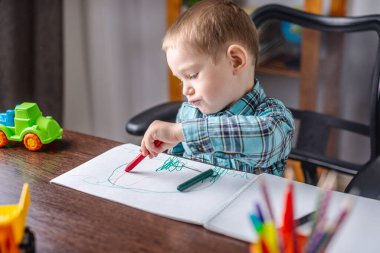 Sevimli çocuk masadaki bir albümde tebeşirle kağıt üzerine resim çiziyor. Anaokulu eğitimi ve yaratıcılığın gelişimi kavramı