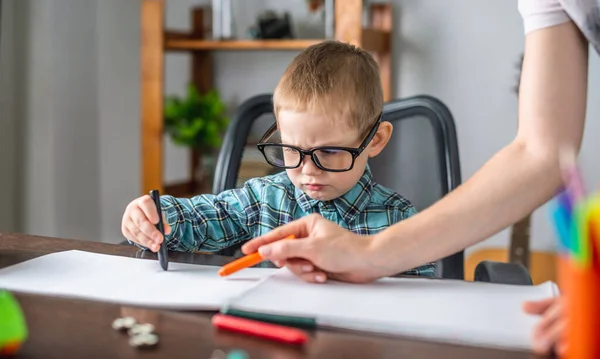 お母さんはかわいい子供がテーブルのアルバムに紙に鉛筆で描くのを手伝っています 就学前教育の概念と創造性の発達 — ストック写真