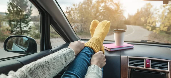 Woman in a car in warm woolen yellow socks on the car dashboard. Cozy autumn weekend trip. The concept of freedom of travel