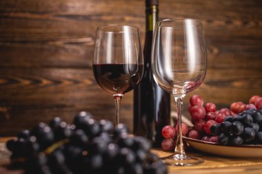 Bir şişe kırmızı şarap, bir bardak ve bir demet üzümle ahşap bir masada. Eklem ve şarap üretimi kavramı