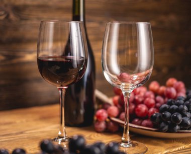 Bir şişe kırmızı şarap, bir bardak ve bir demet üzümle ahşap bir masada. Eklem ve şarap üretimi kavramı