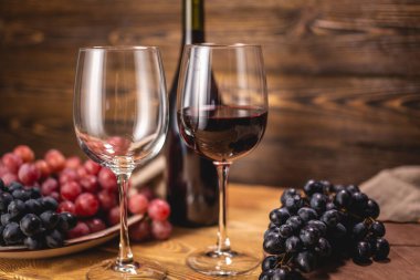 Bir şişe kırmızı şarap, bir bardak ve bir demet üzümle ahşap bir masada. Eklem ve şarap üretimi kavramı