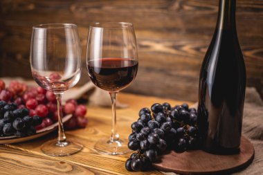 Bir şişe kırmızı şarap, bir bardak ve bir demet üzümle ahşap bir masada. Eklem ve şarap üretimi kavramı