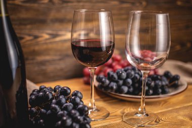 Bir şişe kırmızı şarap, bir bardak ve bir demet üzümle ahşap bir masada. Eklem ve şarap üretimi kavramı