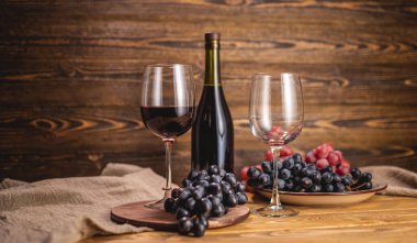 Bir şişe kırmızı şarap, bir bardak ve bir demet üzümle ahşap bir masada. Eklem ve şarap üretimi kavramı