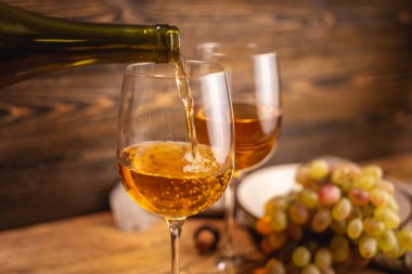 Tahta bir masada bir şişe kuru beyaz şarap, bir bardak ve bir demet üzüm. Eklem ve şarap üretimi kavramı