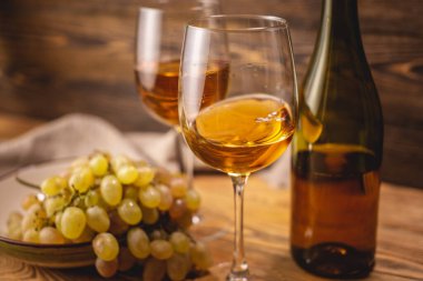 Tahta bir masada bir şişe kuru beyaz şarap, bir bardak ve bir demet üzüm. Eklem ve şarap üretimi kavramı