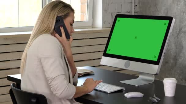 若い女性の受付事務所に電話で話していると彼女のコンピューターのモニターで見て。緑画面モックアップ. — ストック動画