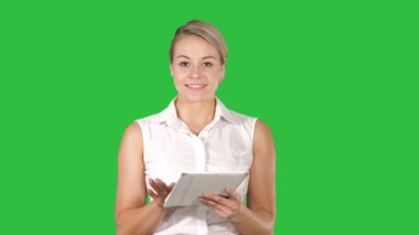Genç gülümseyen iş kadını ile sayfaları çevirme ve Chroma Key bir yeşil ekranda kamera isteyen tablet bilgisayar.