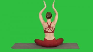 Lotus poz, birleştirme Elleri başının üstünde a yeşil perde, Chroma Key üstünde oturan genç sportif kadın.