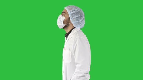 Bonito médico vestindo seu uniforme e vestindo uma máscara ele está andando em uma tela verde, Chroma Key . — Vídeo de Stock