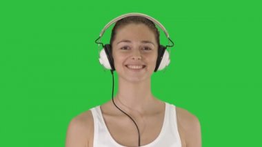 Müzik, insan ve teknoloji kavramı - yeşil ekranda Chroma Key yürüyüş kulaklık ile mutlu gülümseyen kadın.