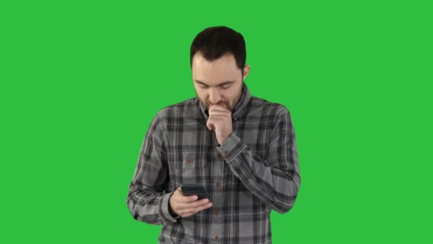 Sad young man walking and looking at his mobile phone with his hand on his face on a Green Screen, Chroma Key. — Stock Video