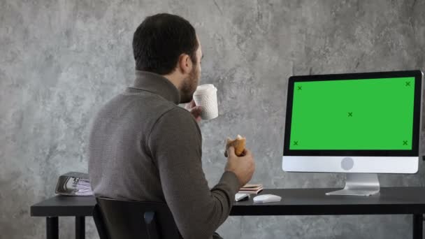 Homem de negócios no escritório tomando café da manhã, almoçando e assistindo algo no Mac, computador. Tela verde Mock-up Display . — Vídeo de Stock