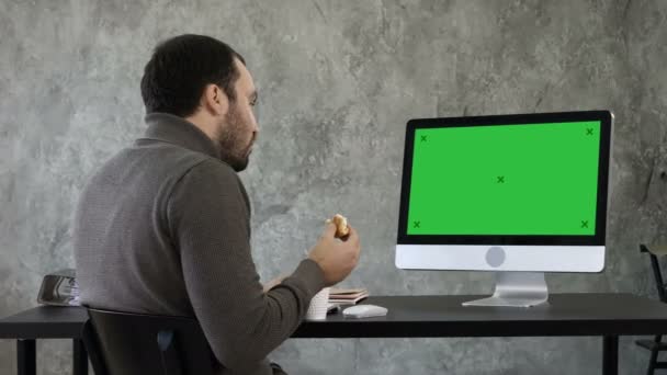 Jongeman verstikking terwijl het eten en kijken naar iets op de computer in het kantoor. Groen scherm Mock-up Display. — Stockvideo