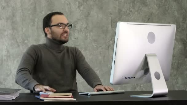 Dühös ember ül az asztalnál a számítógép szürke háttér. — Stock videók