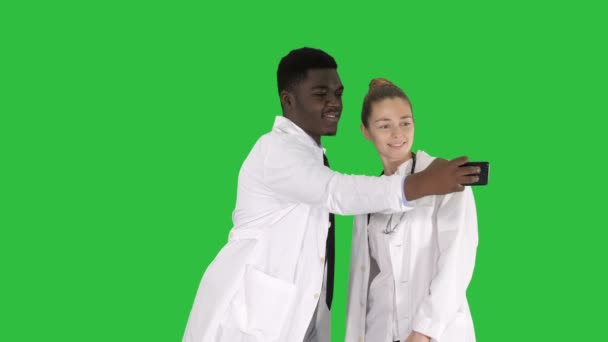 Twee artsen maken selfie met behulp van een smartphone en lachend op een groen scherm, Chromakey. — Stockvideo