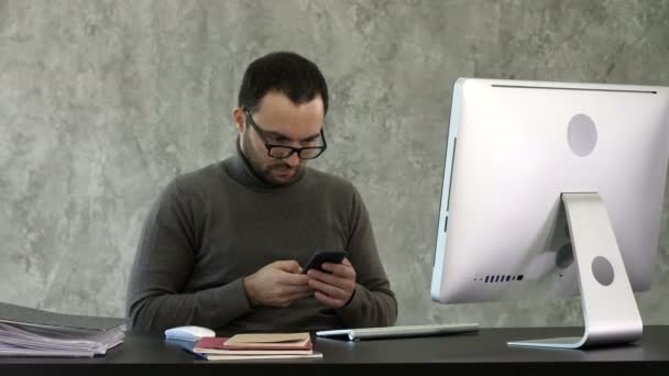 Joven hombre de negocios barbudo que trabaja en una oficina moderna. Hombre mirando en su teléfono inteligente y escribiendo algo . — Vídeo de stock