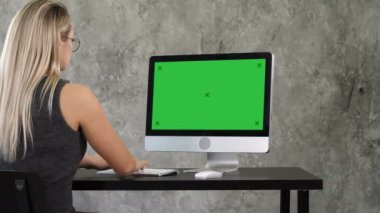 Ofis iç PC masa üzerinde çalışan, yazarak, ekrana bakarak Genç iş kadını. Yeşil perde Mock-up göstermek.