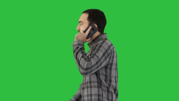 Cooler junger Mann mit Bart, der mit Handy auf grünem Bildschirm läuft und spricht, Chroma-Schlüssel. — Stockvideo