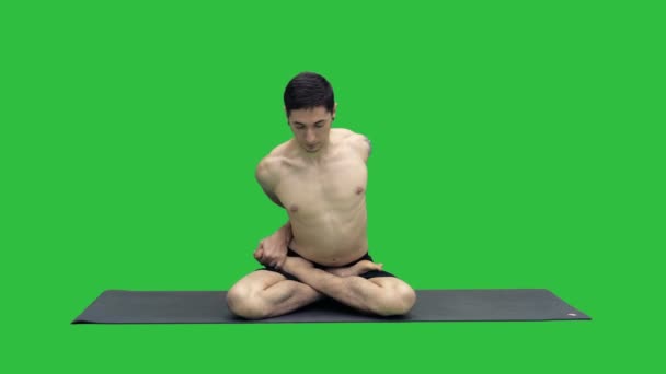 Deportivo joven hermoso que practica yoga, sentado con las piernas cruzadas en Adho Mukha Padmasana, inclinándose hacia adelante en la variación de la postura del loto en una pantalla verde, clave de croma . — Vídeo de stock