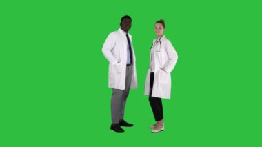 İki beyaz ve afro Amerikan gülümseyen Chroma anahtar yeşil ekranda kamera isteyen ayakta doktorlar.