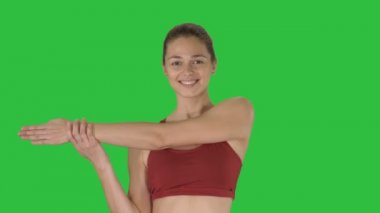 Güzel genç kadın bir yeşil ekranda Chroma Key yürürken germe egzersizleri yapıyor germe yapmak egzersizleri.