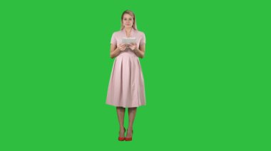 Kameraya bakarak ve bir yeşil ekran, Chroma anahtar üstünde belgili tanımlık etiket sayfaları veya puching düğmeleri açma elinde tablet sahip pembe oldukça büyüleyici emin moda kadın.