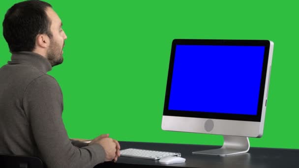 Ung affärsman ringer videosamtal på sin dator på en grön skärm, Chroma Key. Mock-up-blå skärm. — Stockvideo