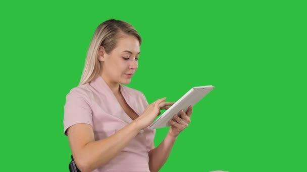 Frau sitzt vor Tablet-PC und lächelt auf grünem Bildschirm, Chroma-Schlüssel. — Stockvideo