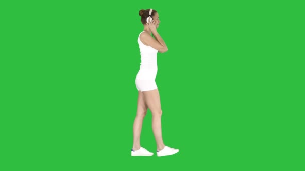 Женщина в белой рубашке слушает музыку с помощью наушников и ходит по зеленому экрану, Chroma Key . — стоковое видео