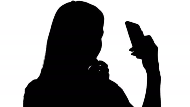 Silhouette Bella giovane donna bionda che sta dipingendo le labbra con rossetto rosso e guardando nel telefono . — Video Stock