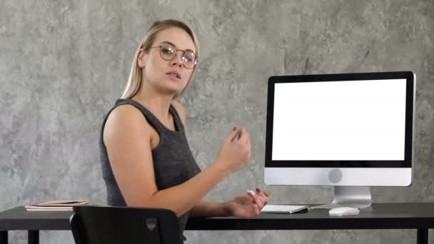 Business κυρία μιλώντας στην κάμερα στο γραφείο δείχνει στην οθόνη του υπολογιστή. Λευκή οθόνη. — Αρχείο Βίντεο
