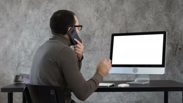 Un uomo che parla al telefono in ufficio e guarda sullo schermo del computer. Display bianco. — Video Stock