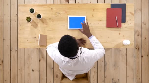 Ein seriöser Arzt, der in seinem Büro mit einem Tablet-Computer Seiten durchblättert. Bluescreen-Attrappe. — Stockvideo