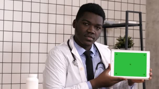 Guapo médico africano serio que presenta el producto en la pantalla del comprimido. Pantalla blanca. — Vídeo de stock