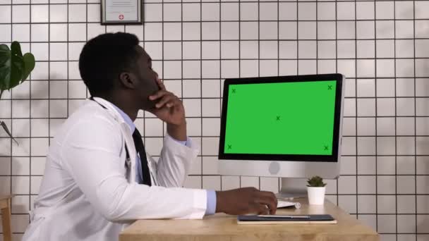 Un joven médico africano mirando el monitor de su computadora. Pantalla blanca . — Vídeos de Stock