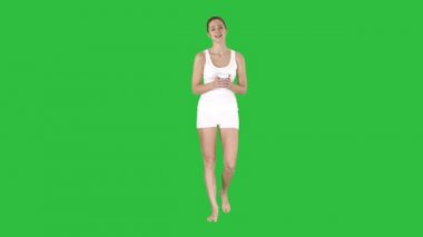 Kadın bir kağıt bardak kahve tutarak ve kamera için Chroma anahtar yeşil ekran konuşurken beyaz spor giyim.