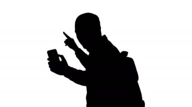 Orta ölçekli yan görüş. Siluet insanlar, yaşam tarzı, doğa ve macera konsepti. Sırt çantalı şık bir genç gezgin elinde akıllı bir telefonla kendini vuruyor ve yolculuğunun video raporunu kaydediyor.