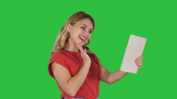 Blond ung tjej med tabletten i handen, att göra ett videosamtal eller videoinspelning, leende på en grön skärm, Chroma Key. — Stockvideo