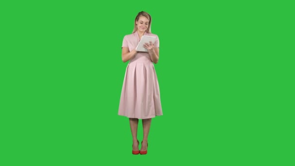 Mooie jonge vrouw in roze jurk holding tablet en op zoek op het op een groen scherm, Chromakey. — Stockvideo